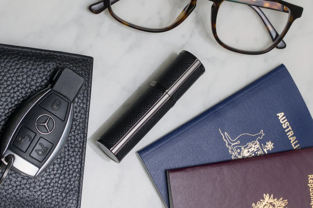 Flâneur Parfum leather travel atomizer alongside passport, Mercedes key, wallet and glasses on marble surface
