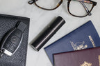 Flâneur Parfum leather travel atomizer alongside passport, Mercedes key, wallet and glasses on marble surface